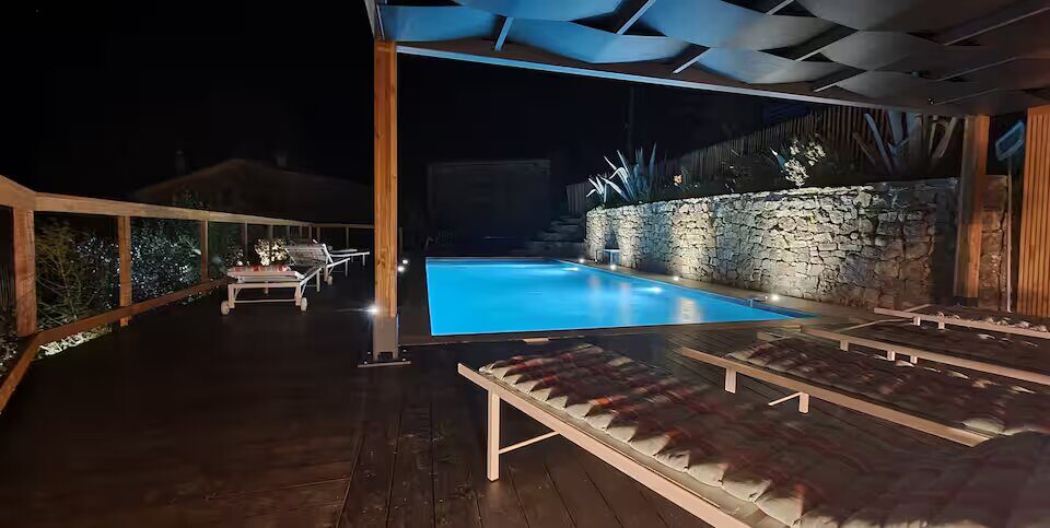 La piscine éclairée à la nuit tombée, sous la pergola